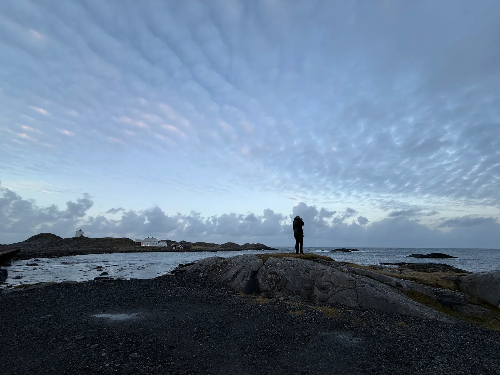 Ein person på eit svaberg, med eit fyr og kystbygningar i bakgrunnen