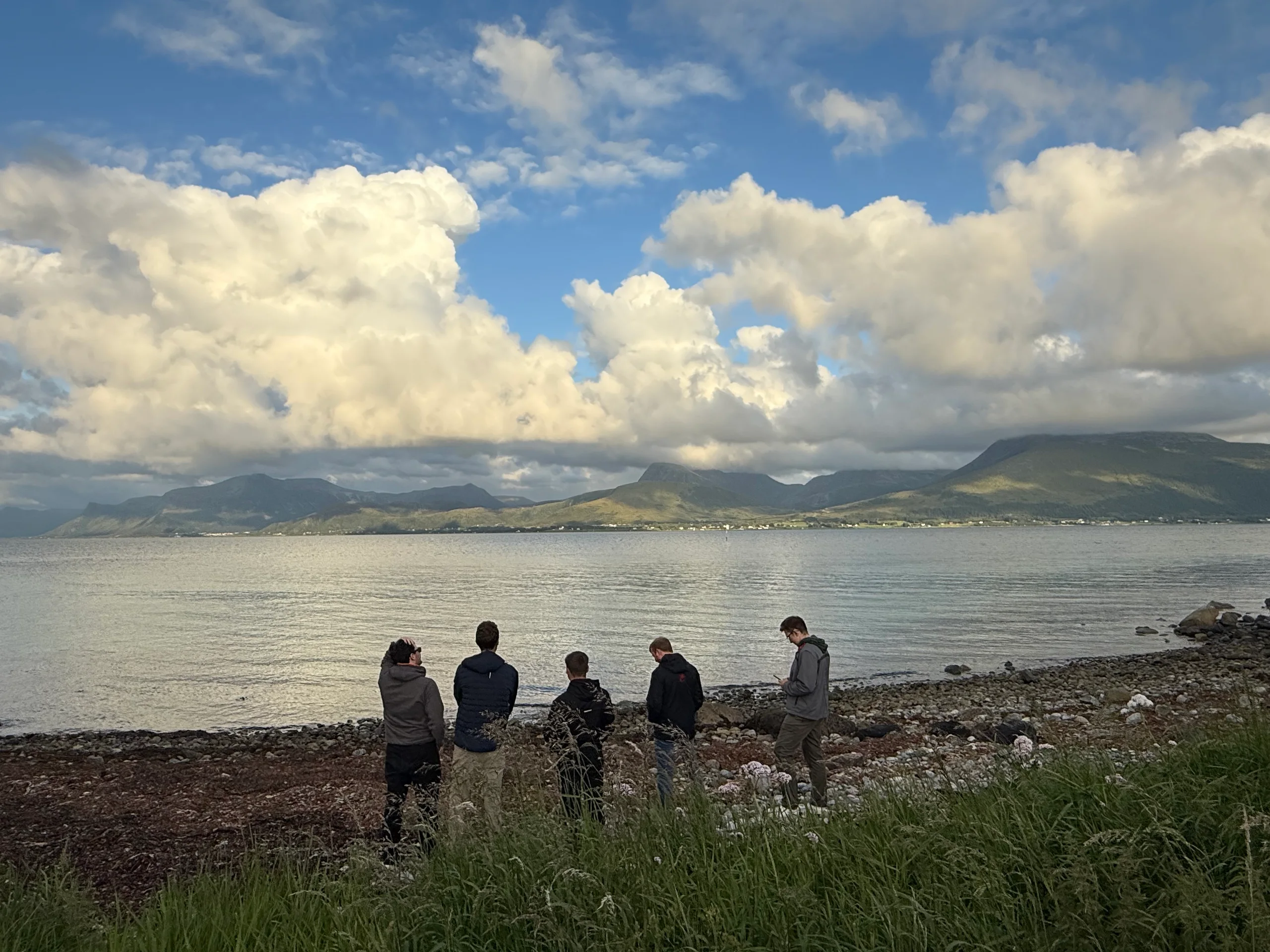 Folk i fjøra med havet og fjella framfor seg